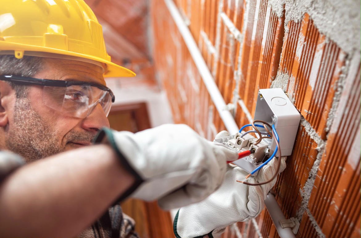 Certified electrician installing wiring into a junction box on site